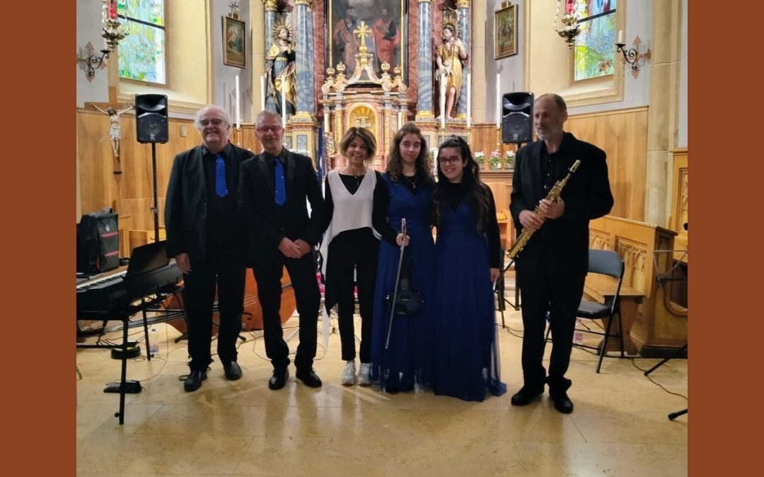 Gruppo di musicisti e organizzatori sul palco di una chiesa ad Arabba al termine del concerto Stella e la Regina delle Dolomiti, agosto 2026